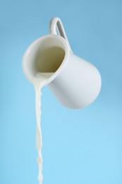 Photo of Pouring milk from jug on light blue background