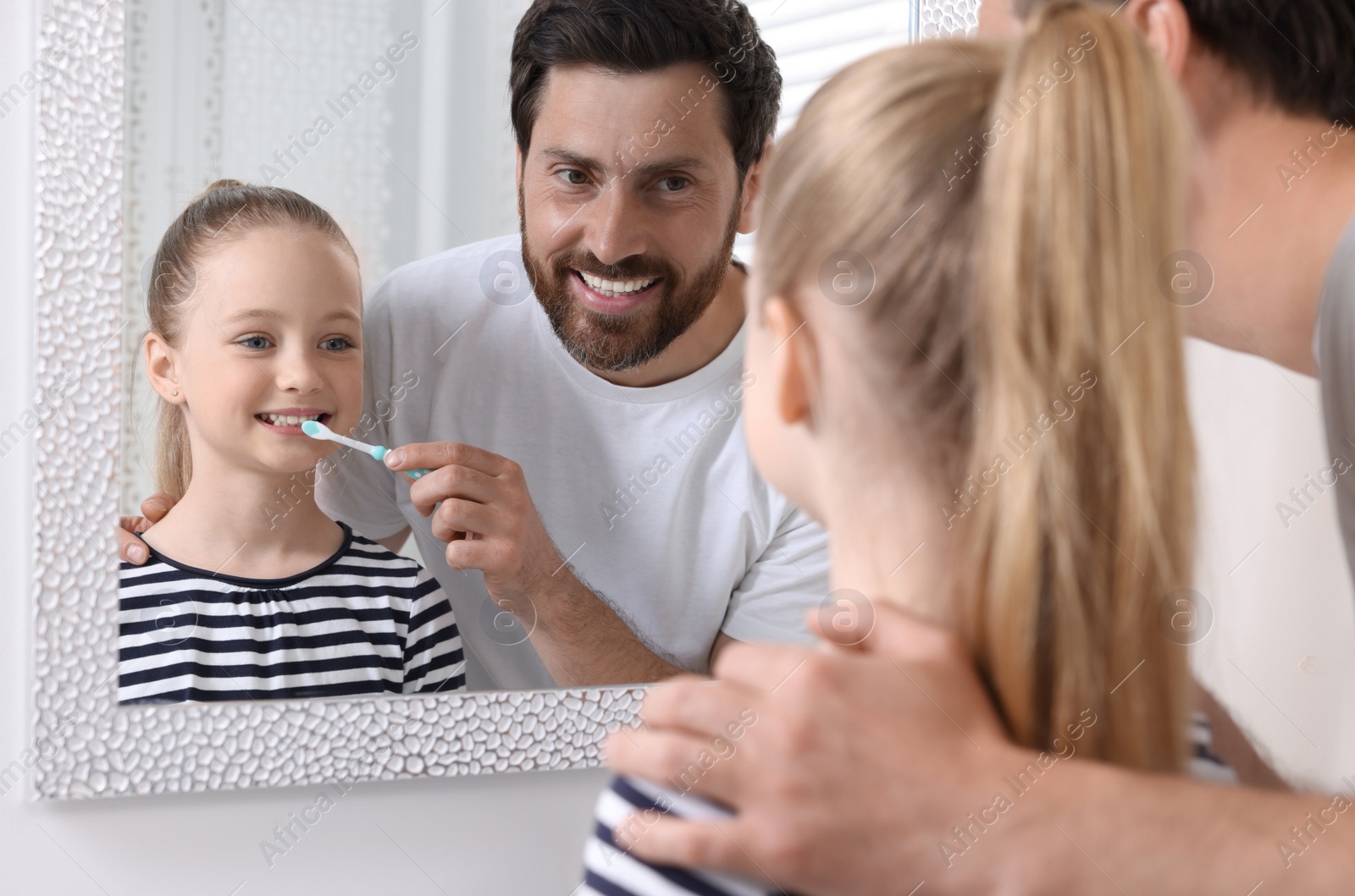 Photo of Father helping his daughter to brush teeth near mirror indoors