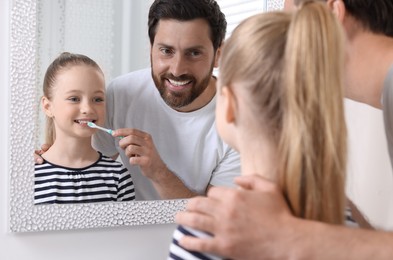 Father helping his daughter to brush teeth near mirror indoors