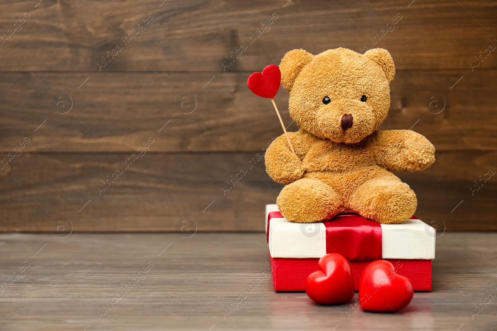 Photo of Cute teddy bear with red hearts and gift box on wooden table, space for text. Valentine's day celebration