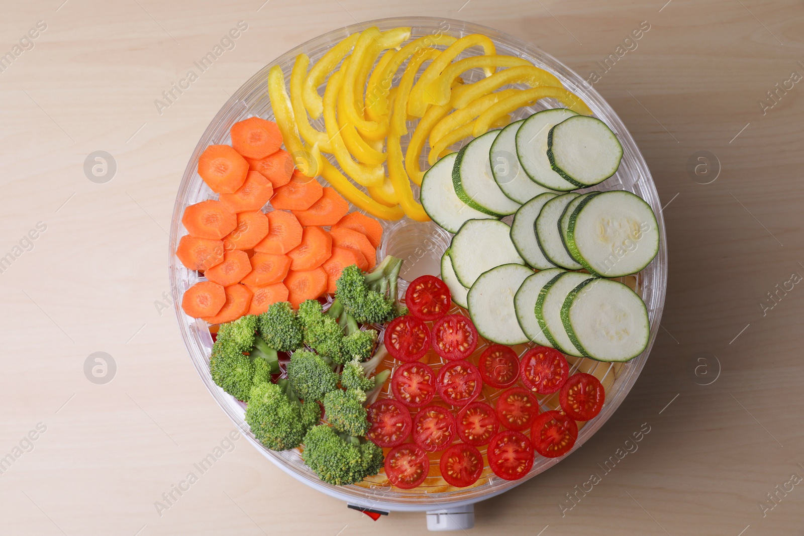 Photo of Cut vegetables in fruit dehydrator machine on wooden table, top view