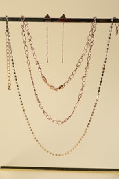 Photo of Stand with different metal chains and earrings on beige background. Luxury jewelry
