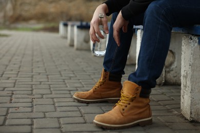 Photo of Addicted man with alcoholic drink on bench outdoors, closeup. Space for text