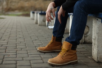 Addicted man with alcoholic drink on bench outdoors, closeup. Space for text