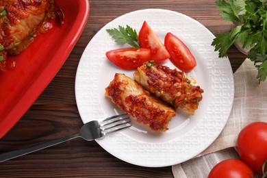 Photo of Delicious stuffed cabbage rolls with tomatoes served on wooden table, flat lay