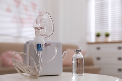 Modern nebulizer with face mask and liquid medicine on white table indoors. Inhalation equipment