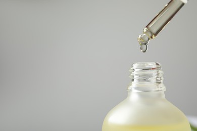Dripping hydrophilic oil into bottle on grey background, closeup. Space for text