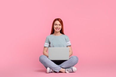 Photo of Smiling young woman working with laptop on pink background