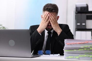 Overwhelmed man sitting at table with laptop and documents in office