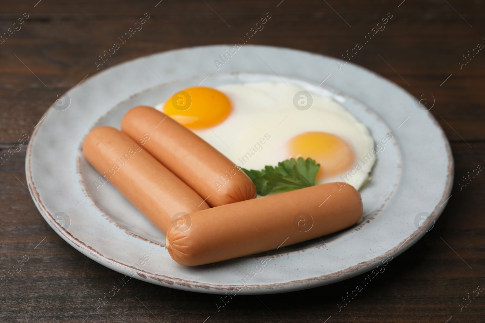 Photo of Delicious boiled sausages, fried eggs and parsley on wooden table, closeup