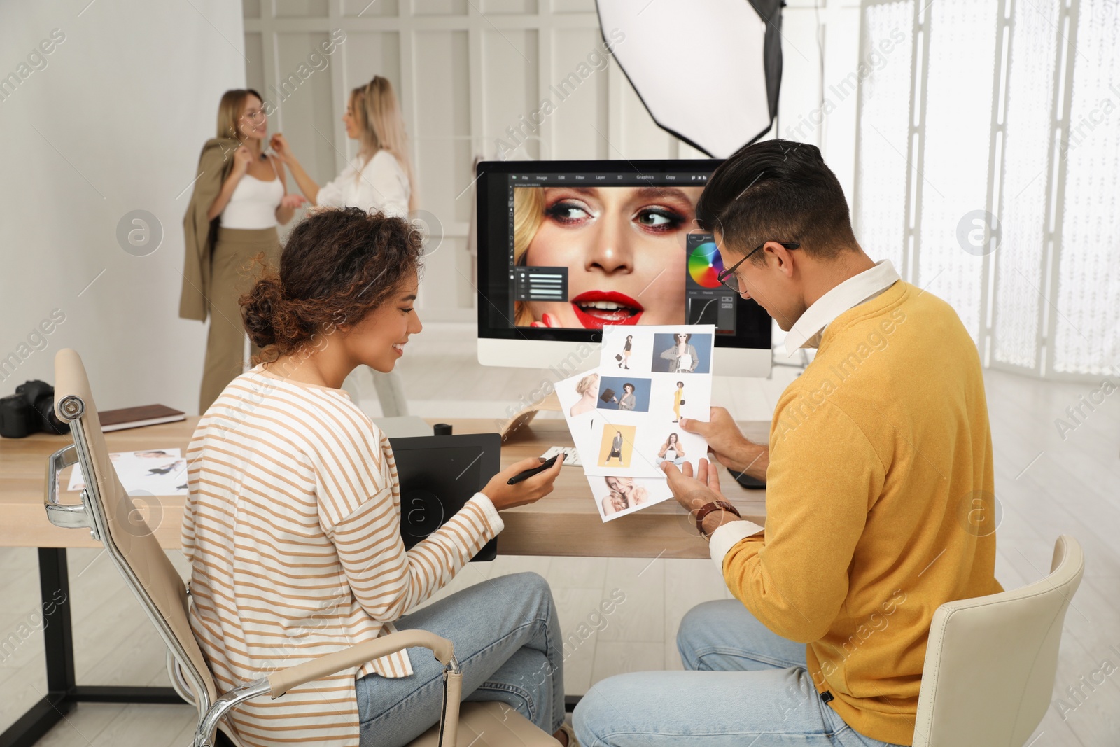 Photo of Professional retoucher with colleague working at desk in photo studio