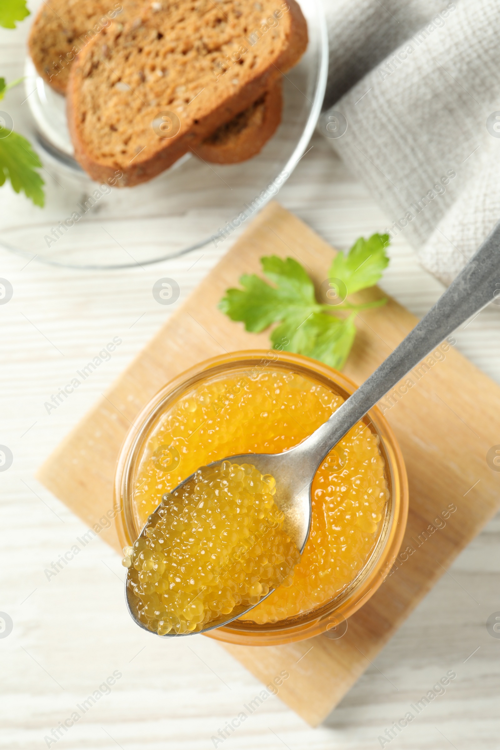 Photo of Fresh pike caviar in glass jar, parsley, bread and spoon on white wooden table, flat lay