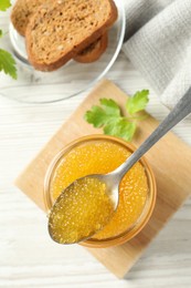 Fresh pike caviar in glass jar, parsley, bread and spoon on white wooden table, flat lay