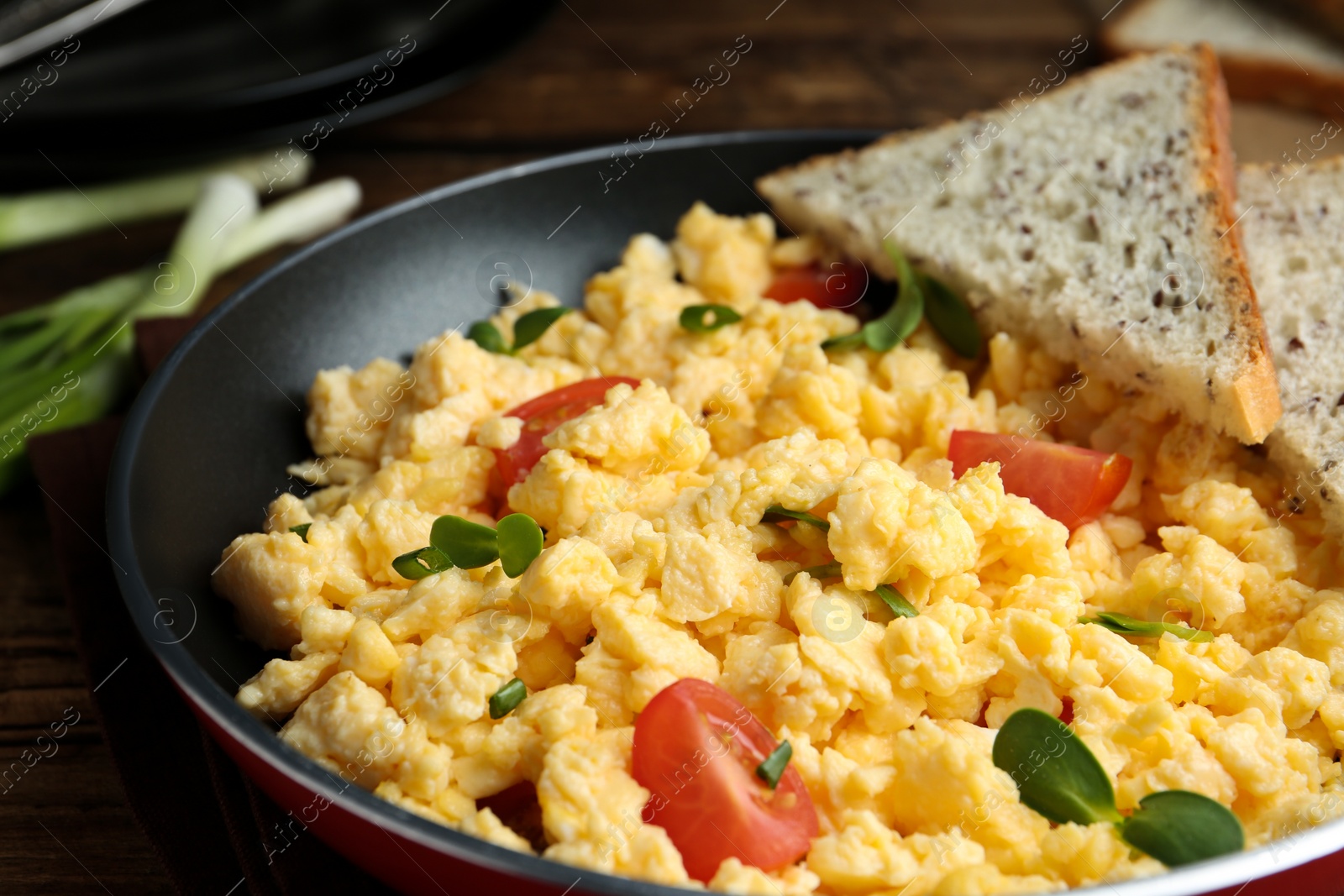 Photo of Tasty scrambled eggs with sprouts, cherry tomato and bread in frying pan on table, closeup