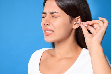 Photo of Young woman cleaning ear with cotton swab on light blue background, closeup