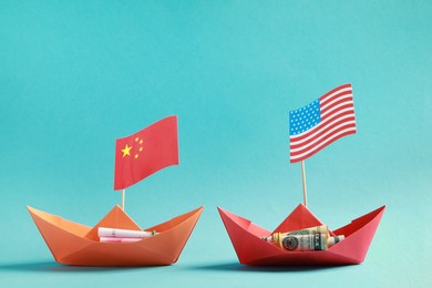 Photo of Paper boats with money and national flags on turquoise background. Trade war