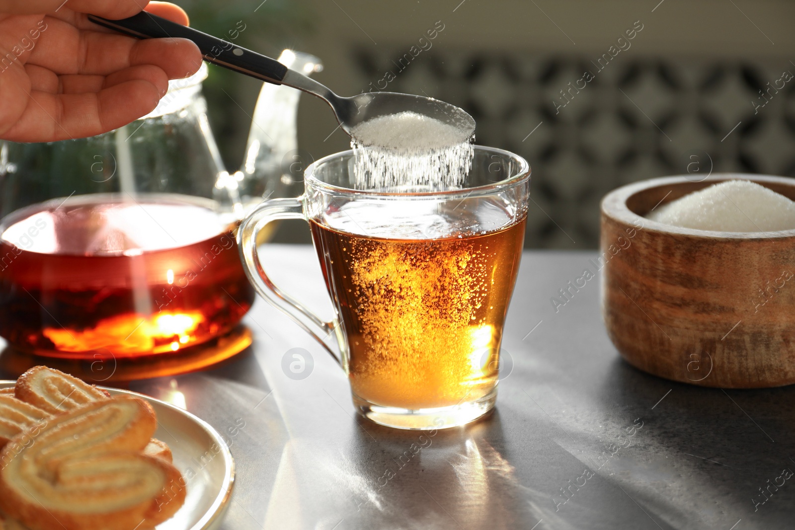 Photo of Woman adding sugar into cup of tea at dark table, closeup