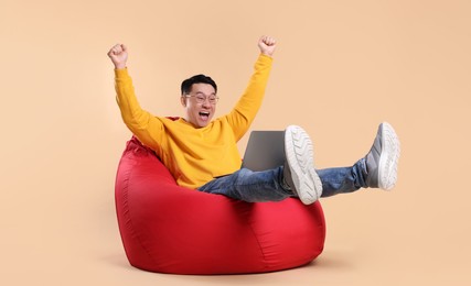 Photo of Emotional man with laptop sitting in beanbag chair against beige background