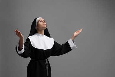 Photo of Nun praying to God on grey background. Space for text
