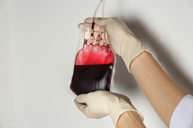 Photo of Woman holding blood for transfusion on light background, closeup. Donation concept