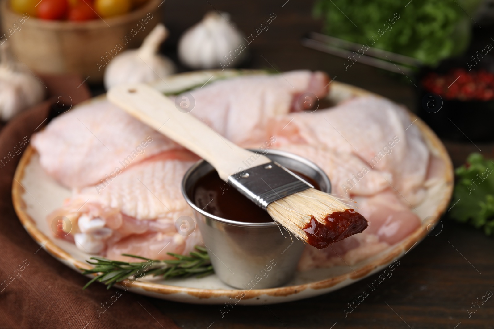 Photo of Plate with fresh marinade, raw chicken and basting brush on wooden table, closeup