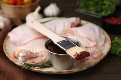 Photo of Plate with fresh marinade, raw chicken and basting brush on wooden table, closeup