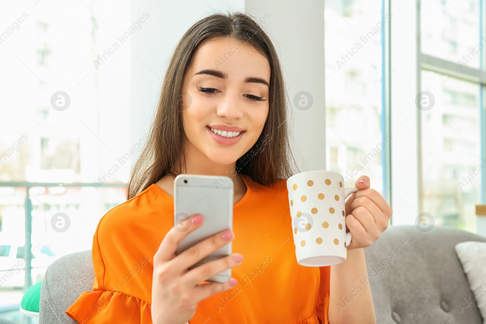 Photo of Young woman with mobile phone drinking coffee at home