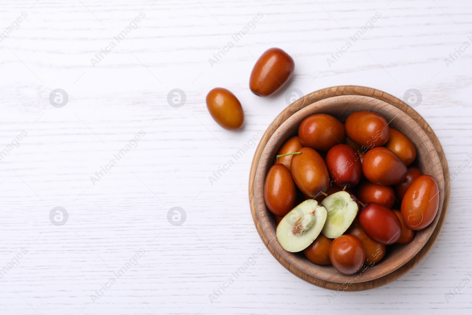Photo of Fresh Ziziphus jujuba fruits with bowl on white wooden table, flat lay. Space for text