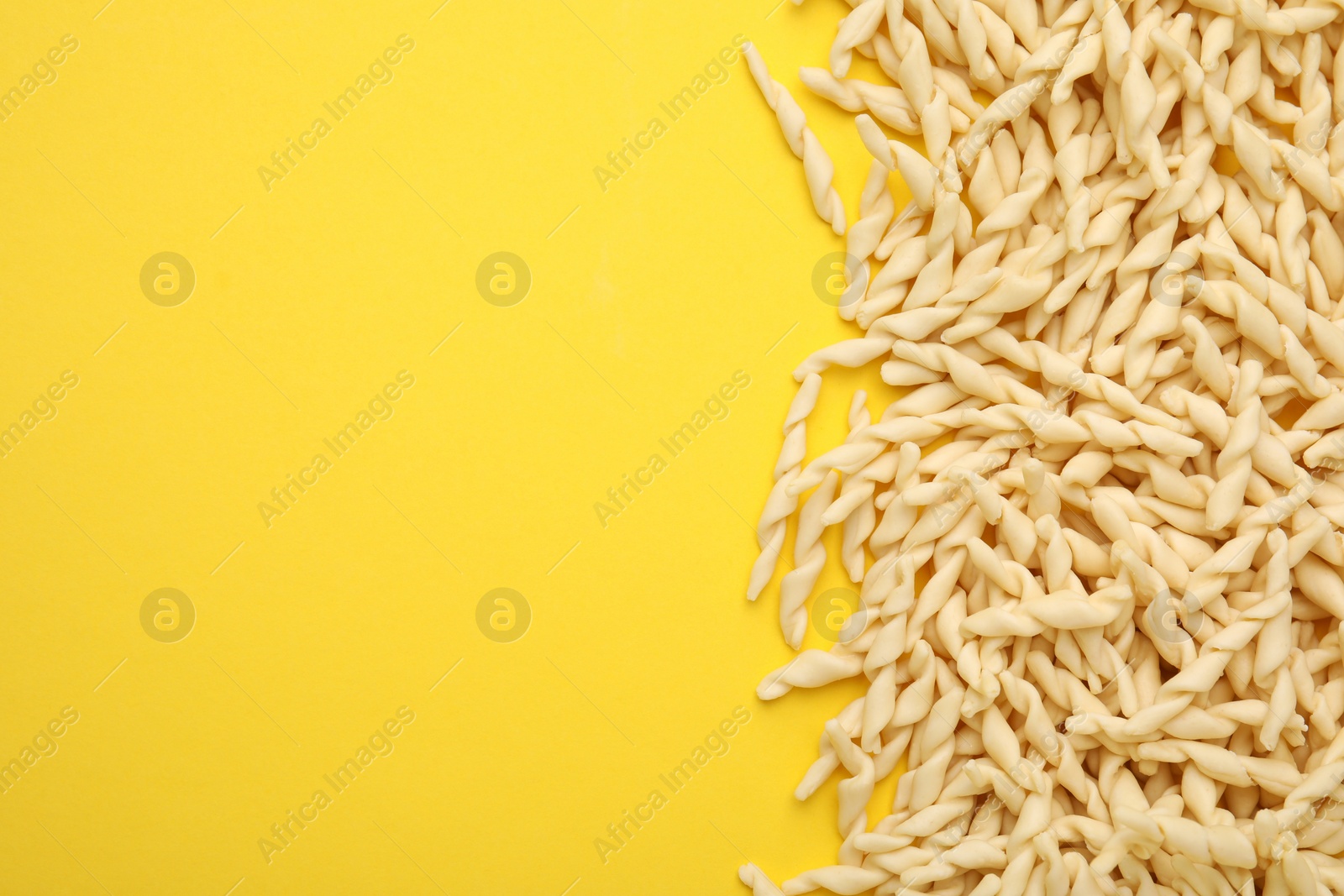 Photo of Uncooked trofie pasta on yellow background, flat lay. Space for text