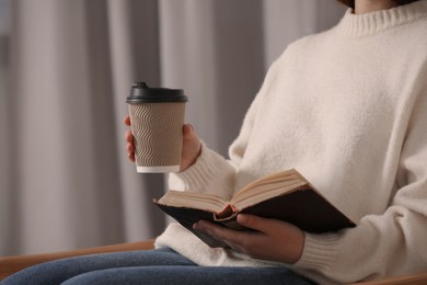 Woman holding takeaway cardboard cup and book indoors, closeup. Coffee to go