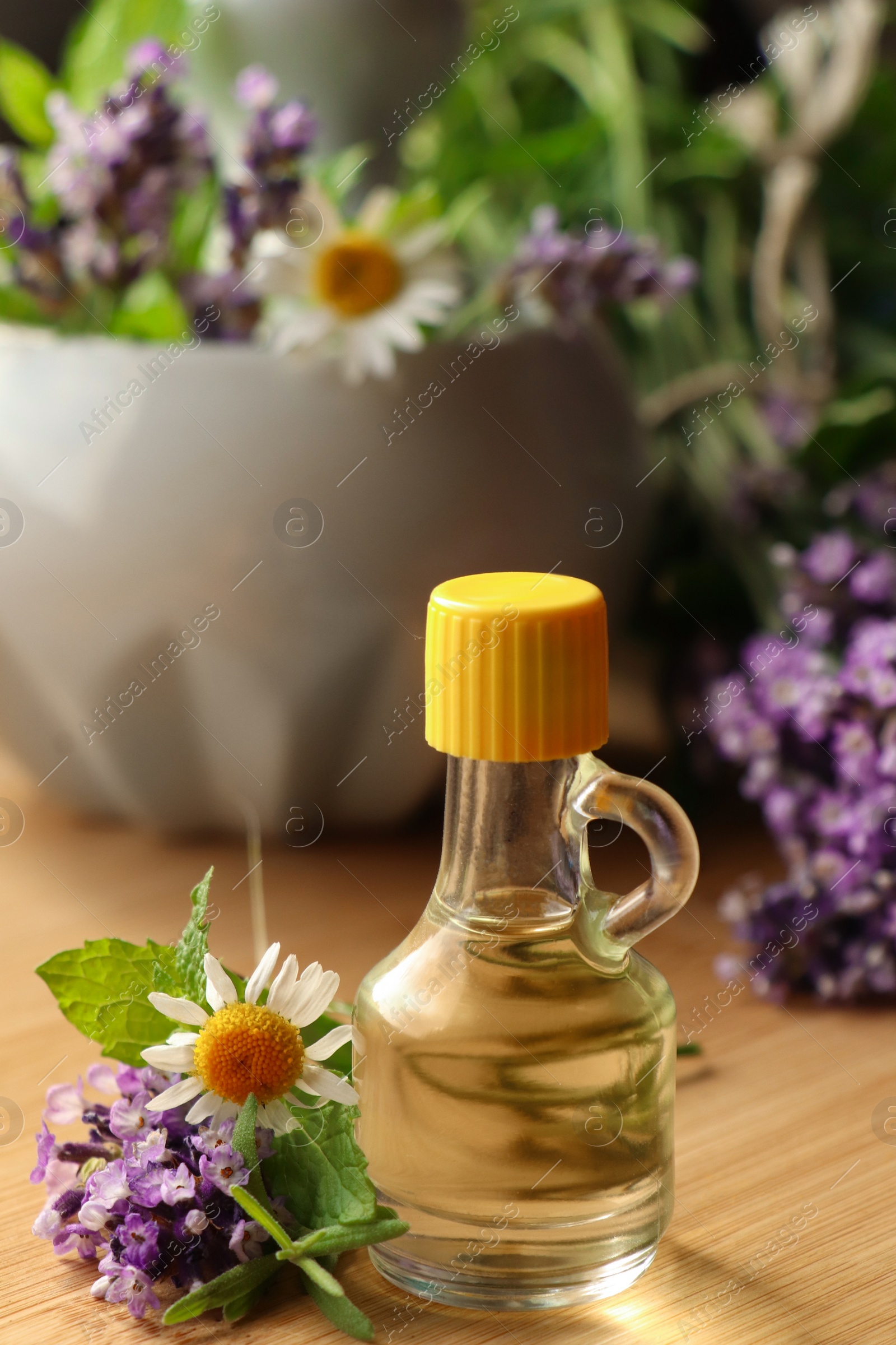 Photo of Bottle of natural lavender essential oil near mortar with flowers on wooden table