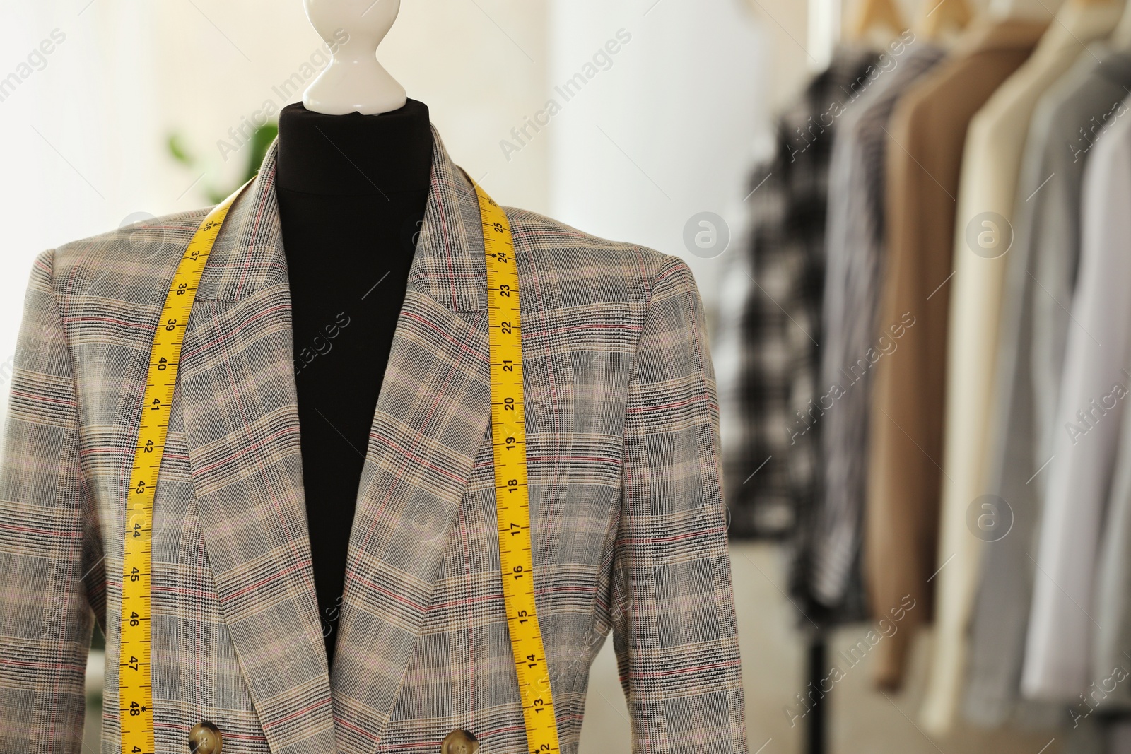 Photo of Mannequin with jacket and measuring tape in tailor shop, space for text