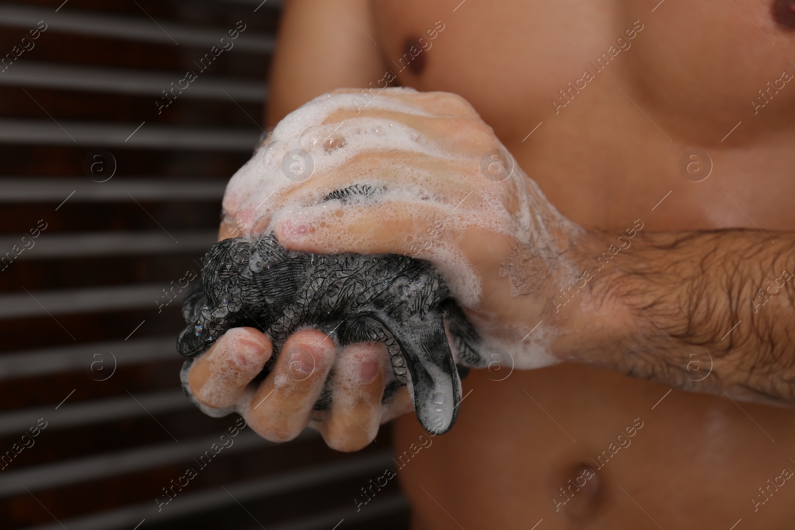 Photo of Man with mesh pouf taking shower at home, closeup
