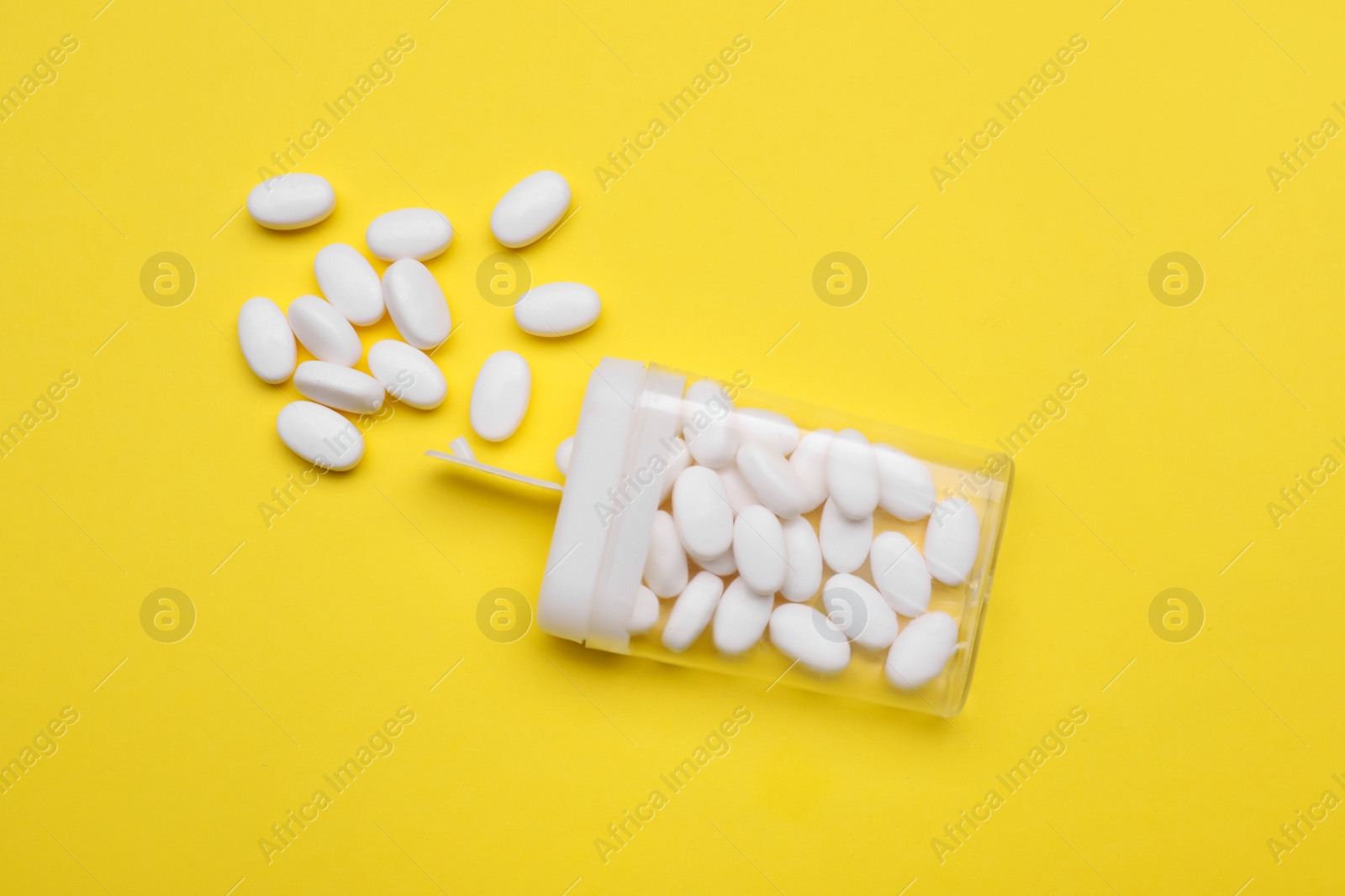 Photo of Tasty dragee candies and container on yellow background, flat lay