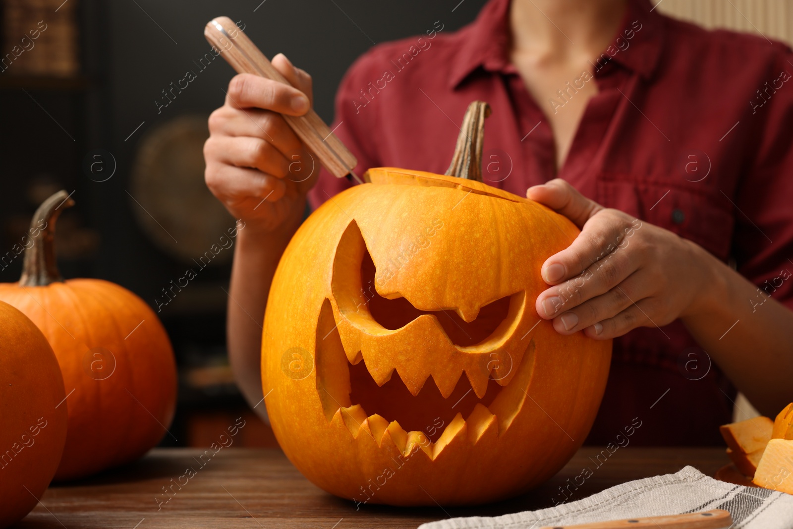 Photo of Woman carving pumpkin for Halloween at wooden table indoors, closeup