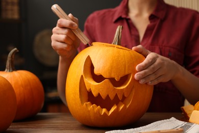 Woman carving pumpkin for Halloween at wooden table indoors, closeup