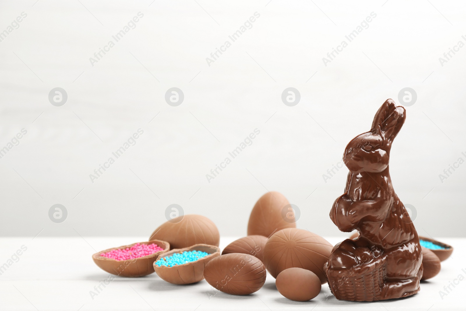 Photo of Chocolate Easter bunny and eggs on white table. Space for text