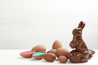 Photo of Chocolate Easter bunny and eggs on white table. Space for text