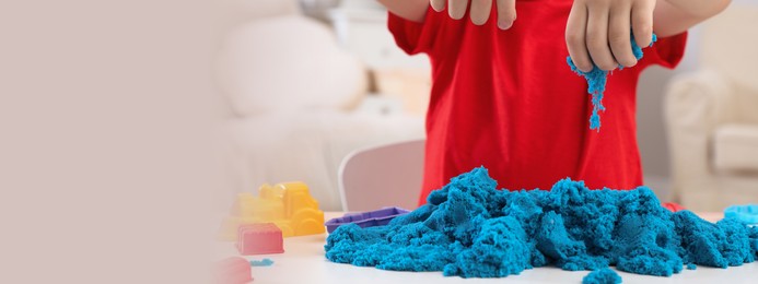 Image of Little boy playing with bright kinetic sand at table indoors, closeup view with space for text. Banner design