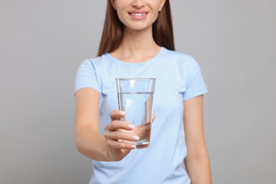 Photo of Healthy habit. Woman holding glass with fresh water against grey background, focus on hand