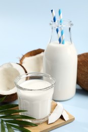 Photo of Delicious vegan milk, coconuts and leaf on light blue background