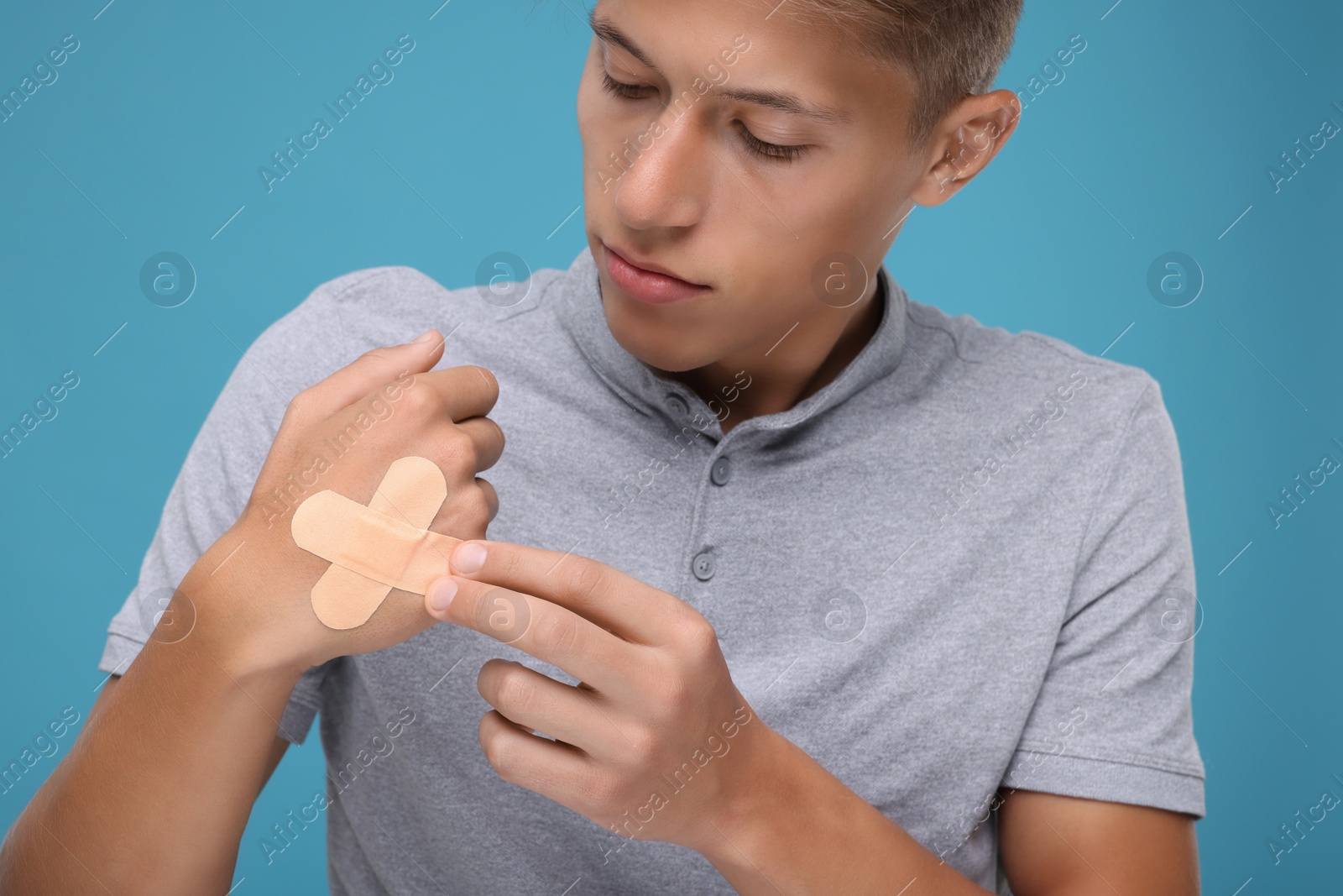 Photo of Handsome man putting sticking plasters onto hand on light blue background