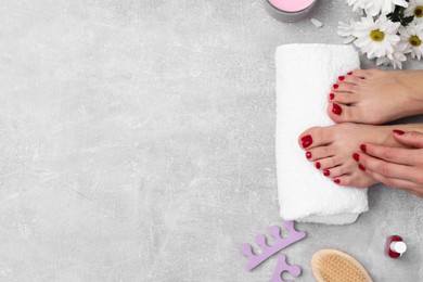 Woman with stylish red toenails after pedicure procedure, tools and chamomile flowers on grey textured background, top view. Space for text