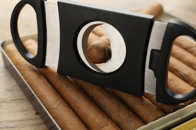 Box of cigars and guillotine cutter on wooden table, closeup