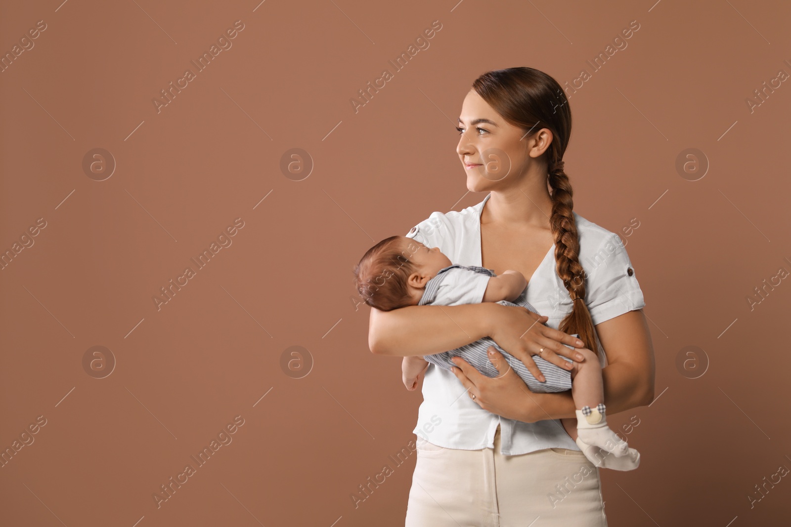 Photo of Mother holding her cute newborn baby on brown background, space for text