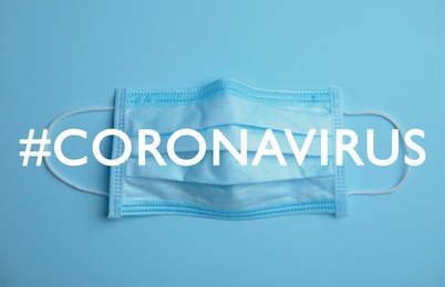 Image of Hashtag Coronavirus and medical mask on light blue background, top view