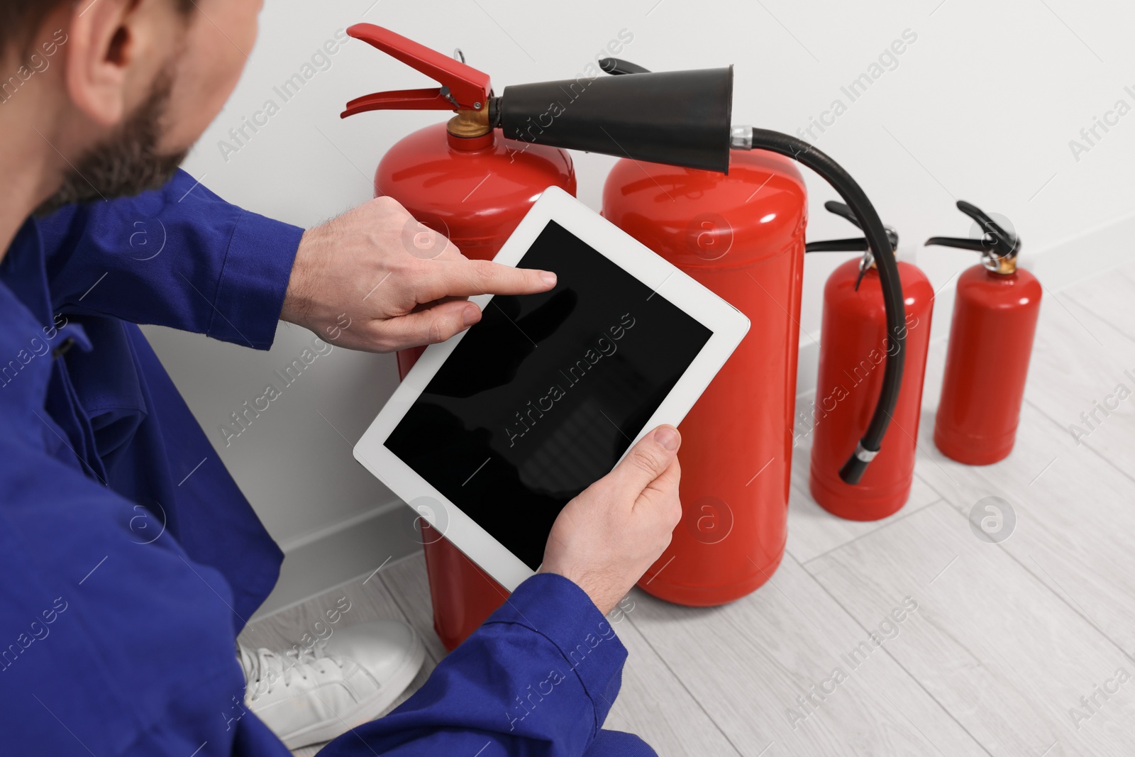 Photo of Man with tablet checking fire extinguishers indoors, closeup