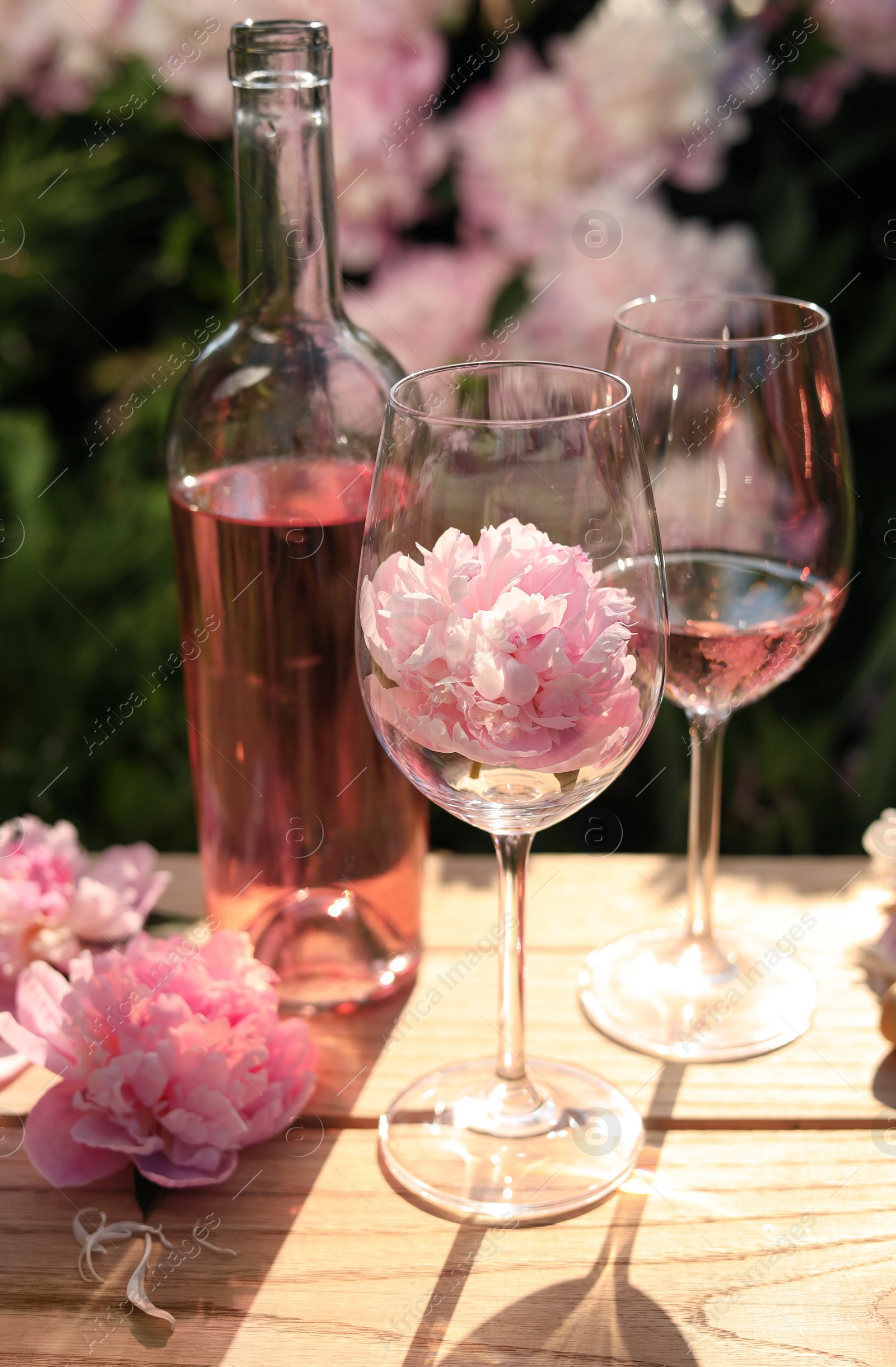 Photo of Bottle and glasses of rose wine near beautiful peonies on wooden table in garden