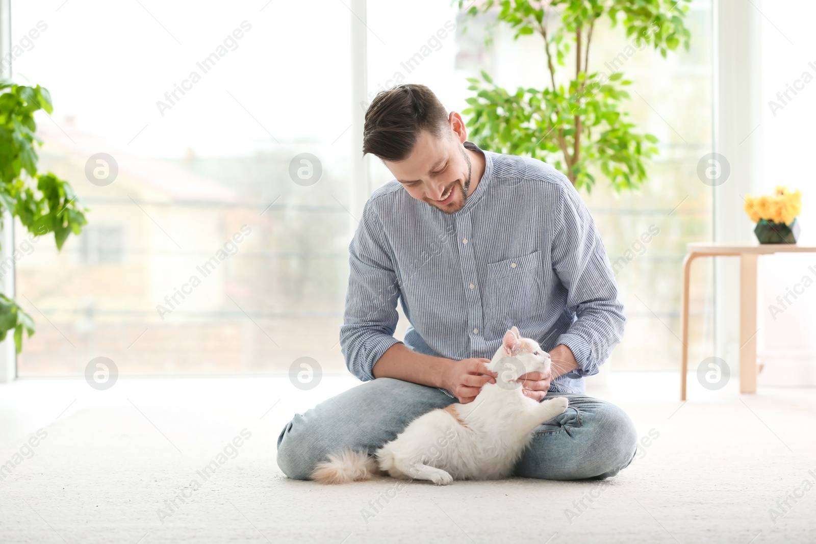 Photo of Young man with cute cat sitting on floor at home