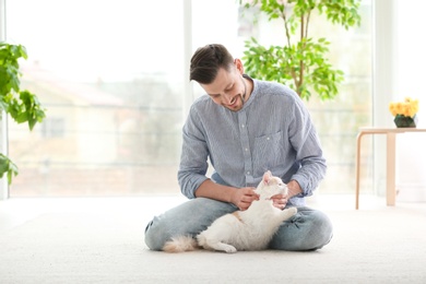 Young man with cute cat sitting on floor at home